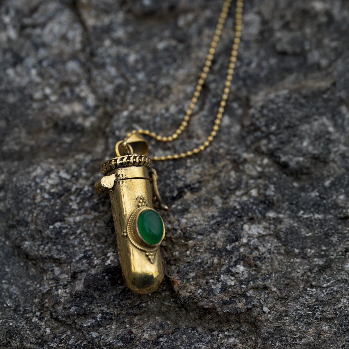Golden brass pendant with a green gemstone on a rocky surface