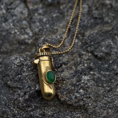Golden brass pendant with a green gemstone on a rocky surface