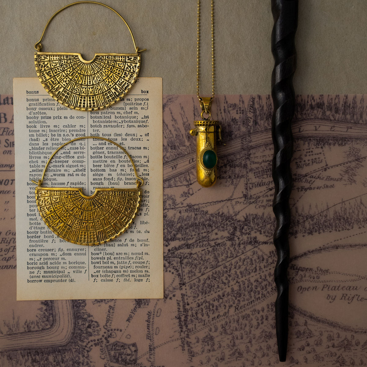 Golden brass earrings and pendant on an old book with a black wooden wand