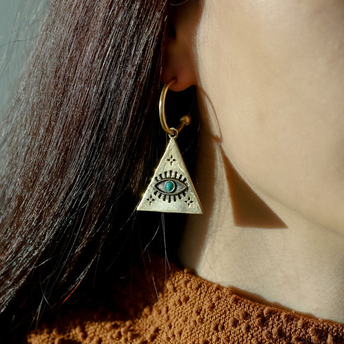 Woman wearing a triangle-shaped earring with an eye design and turquoise stone