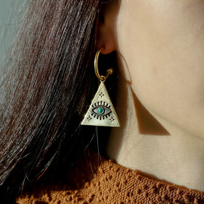 Woman wearing a triangle-shaped earring with an eye design and turquoise stone