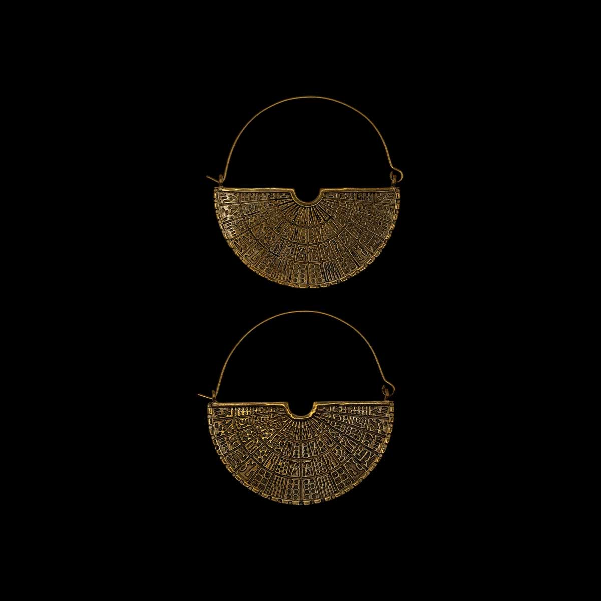 Two brass earrings with intricate designs on a black background