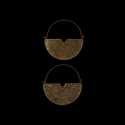 Two brass earrings with intricate designs on a black background