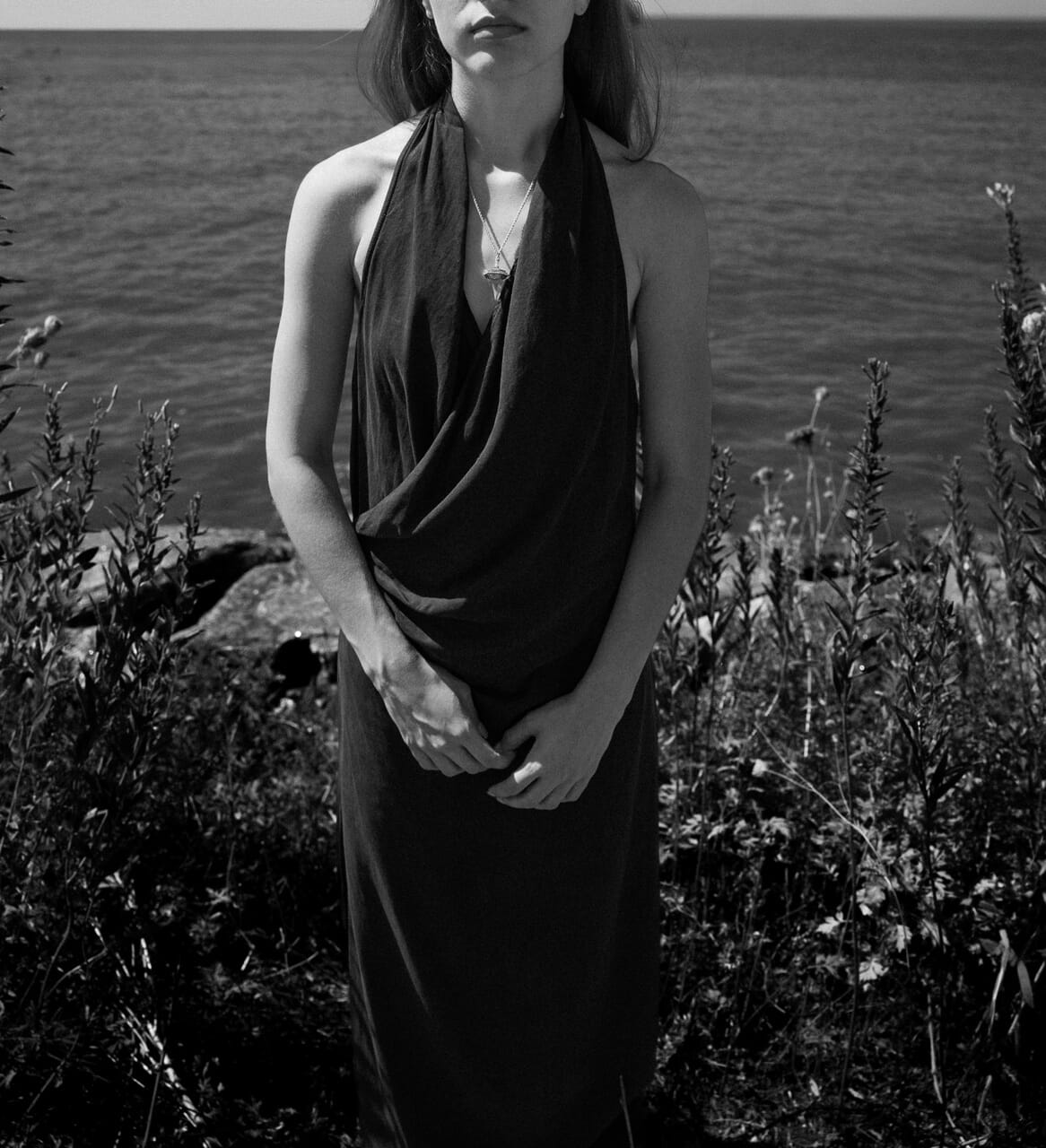 Woman standing by a body of water with plants in the foreground wearing a crystal pendant jewellery
